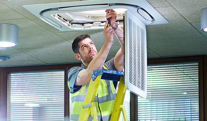 Man on ladder fixing air unit in ceiling